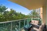 Covered balcony featuring a glass panel railing, paved flooring, and mature foliage