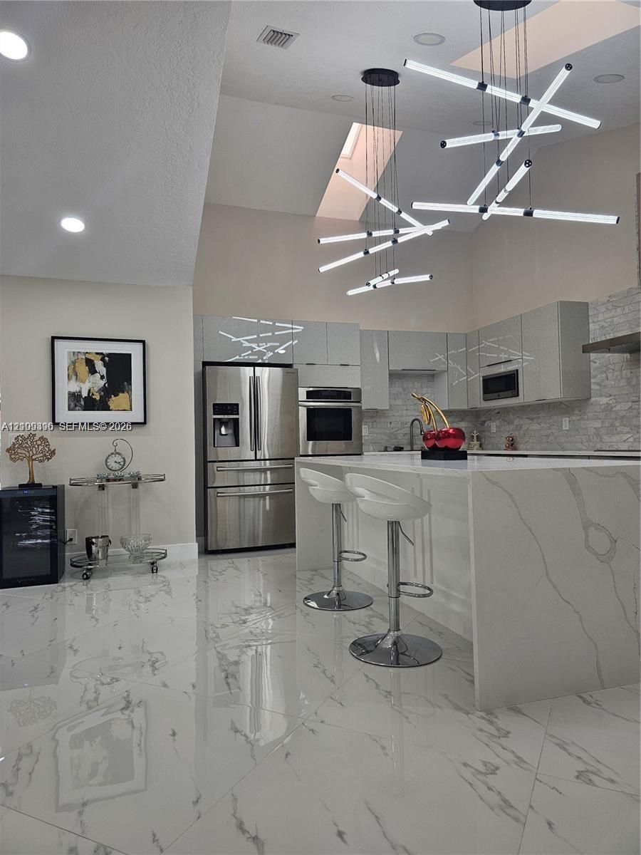 Modern kitchen featuring a waterfall island with stone-finish countertops, high-gloss cabinetry, stainless steel appliances, large-format tile floorin