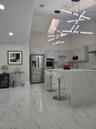 Modern kitchen featuring a waterfall island with stone-finish countertops, high-gloss cabinetry, stainless steel appliances, large-format tile floorin