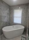 Freestanding soaking tub featuring a chrome floor-mounted faucet and large-format porcelain wall tile with a neutral-toned veined pattern