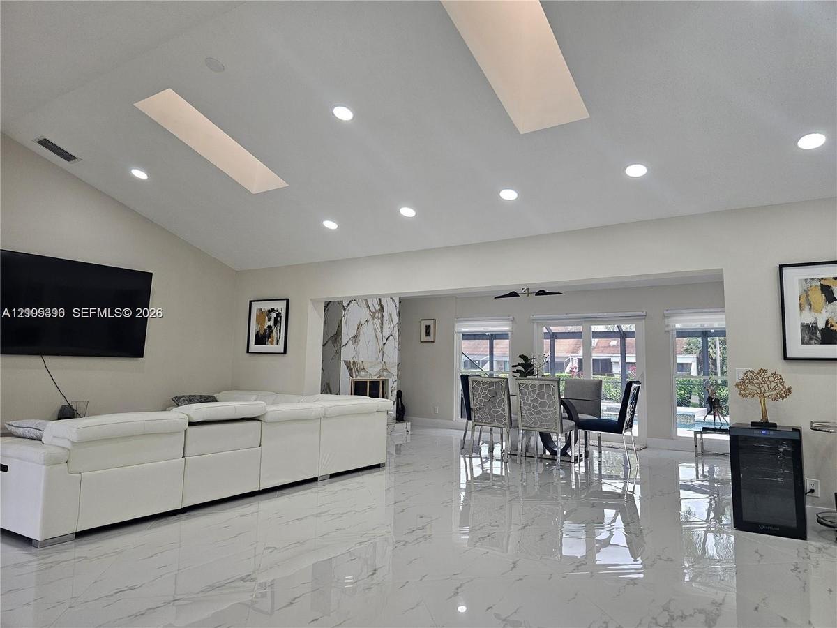 Vaulted ceilings featuring dual skylights, recessed lighting, polished stone-finish flooring, and a floor-to-ceiling stone-surround fireplace