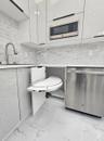 Modern kitchen featuring white flat-panel cabinetry, pull-out corner shelving, stainless steel appliances, stone-patterned backsplash, and matching st