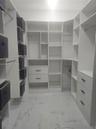 Walk-in closet featuring custom white cabinetry, built-in shelving, integrated dresser drawers with matte black pulls, and large-format polished floor