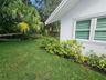 Stucco exterior featuring horizontal louvered windows, manicured lawn, established shrubbery, and mature palm trees