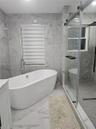 Freestanding soaking tub with a floor-mounted faucet, walk-in shower with a sliding glass door and gray herringbone tile floor, and full-height stone-