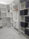 Custom reach-in closet featuring white floor-to-ceiling built-in shelving, integrated hanging rods, two soft-close drawers with matte black hardware, 