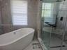 Freestanding oval soaking tub with floor-mounted faucet, walk-in glass-enclosed shower featuring a rainfall showerhead, and large-format wall tiling w