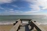 Wood-plank deck with built-in perimeter bench seating and railing, set directly on the sandy shoreline