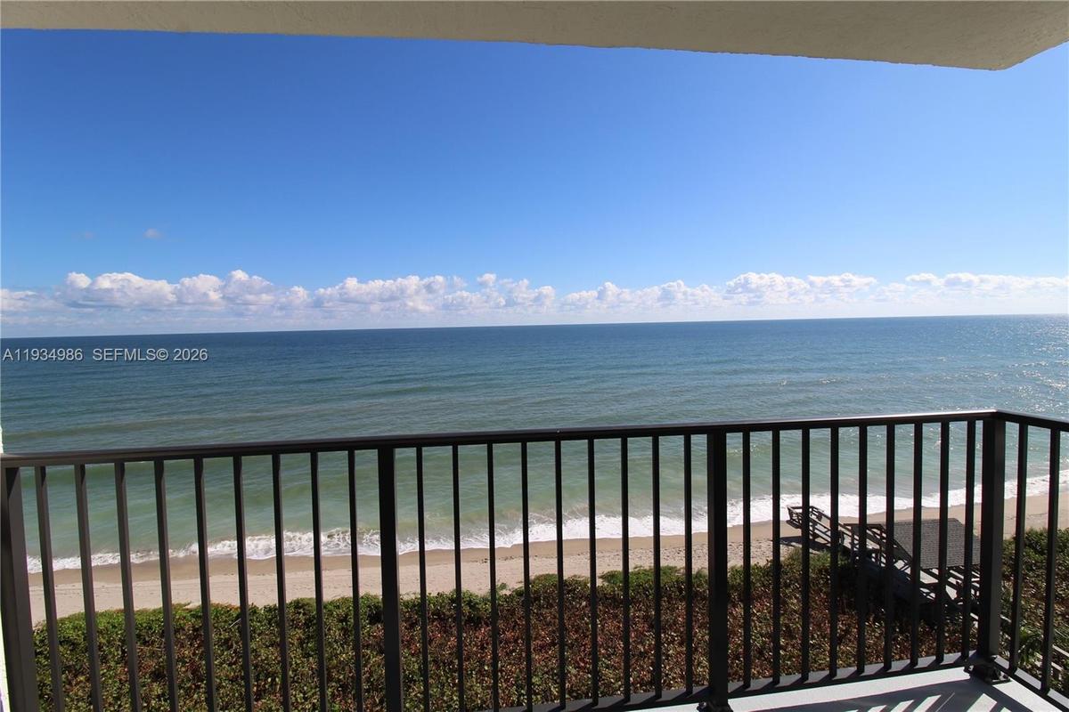 Covered balcony featuring metal railings with direct ocean and sandy beach exposure