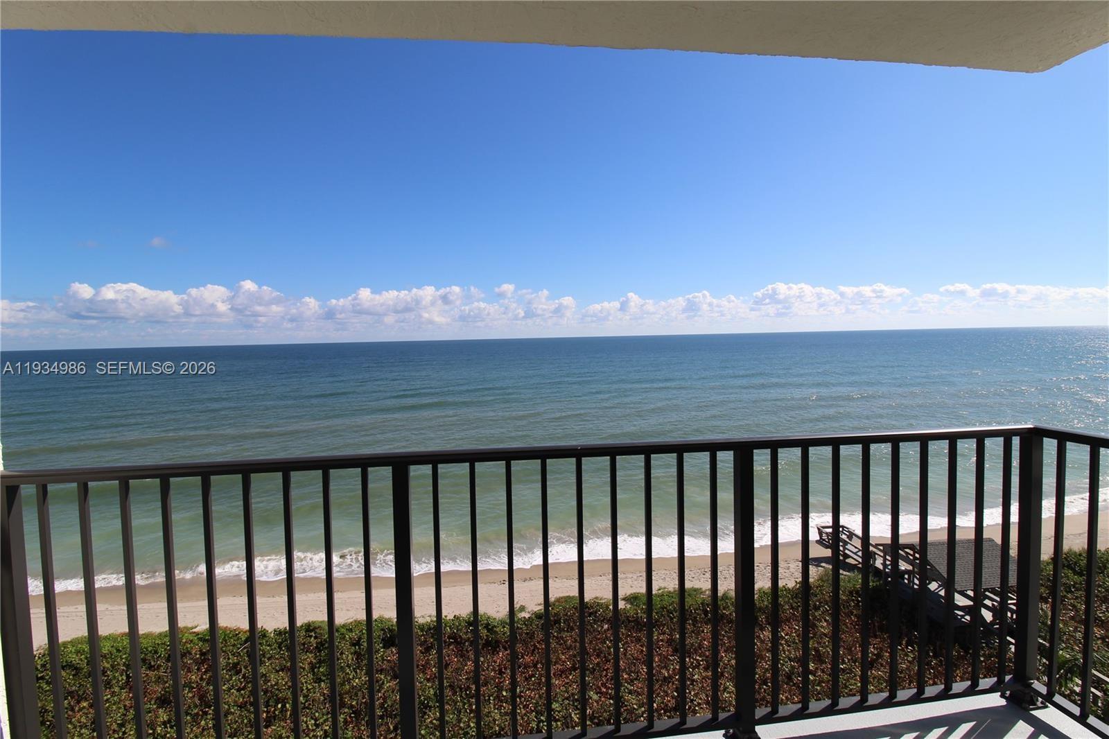 Covered balcony featuring metal railings with direct ocean and sandy beach exposure