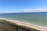 Private balcony featuring metal railings overlooking a sandy shoreline, ocean water, and horizon