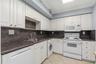 Kitchen featuring white cabinetry, stone countertops, integrated dishwasher, built-in microwave, and tile flooring