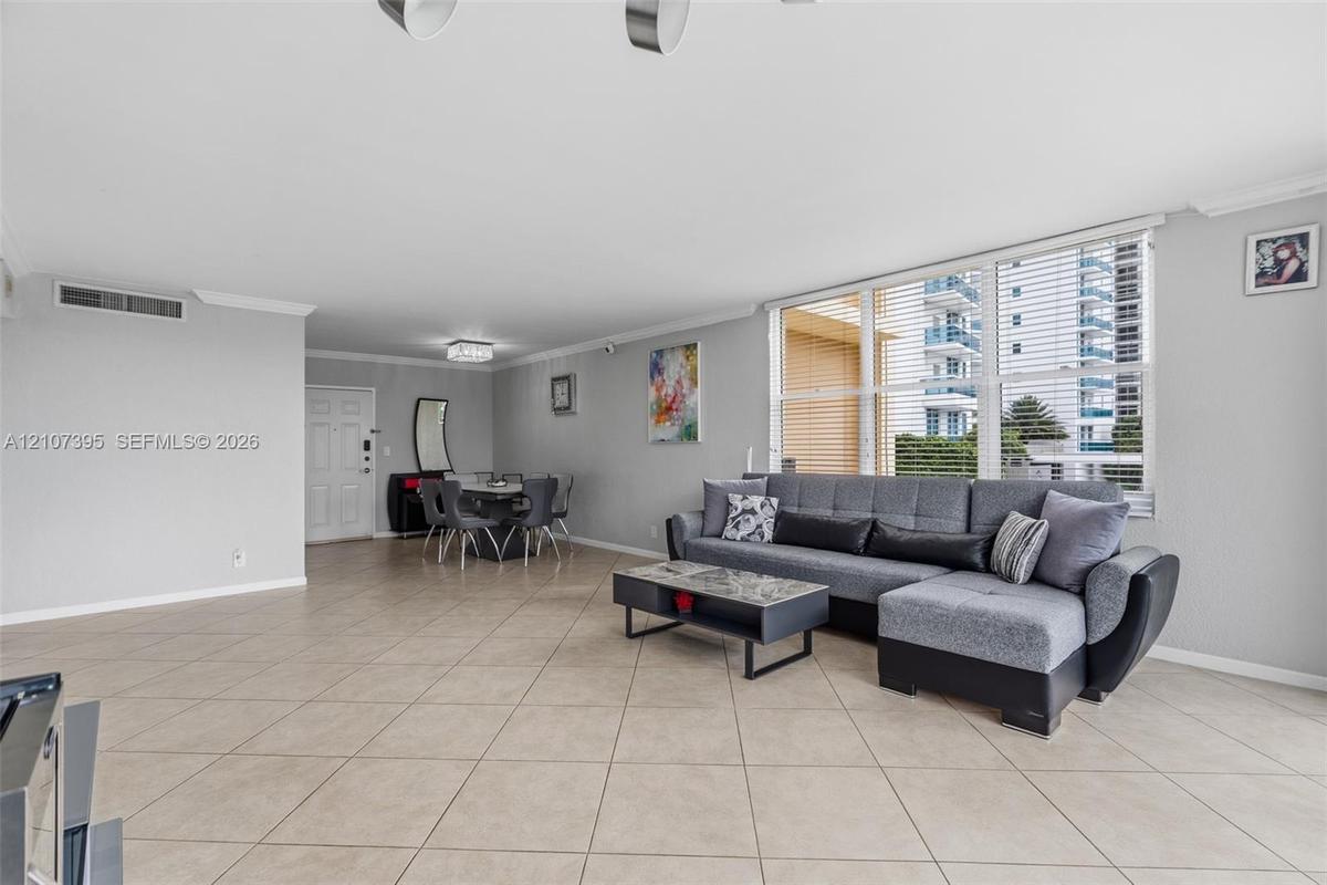 Open-concept living space featuring neutral ceramic tile flooring, crown molding, and floor-to-ceiling windows with horizontal blinds
