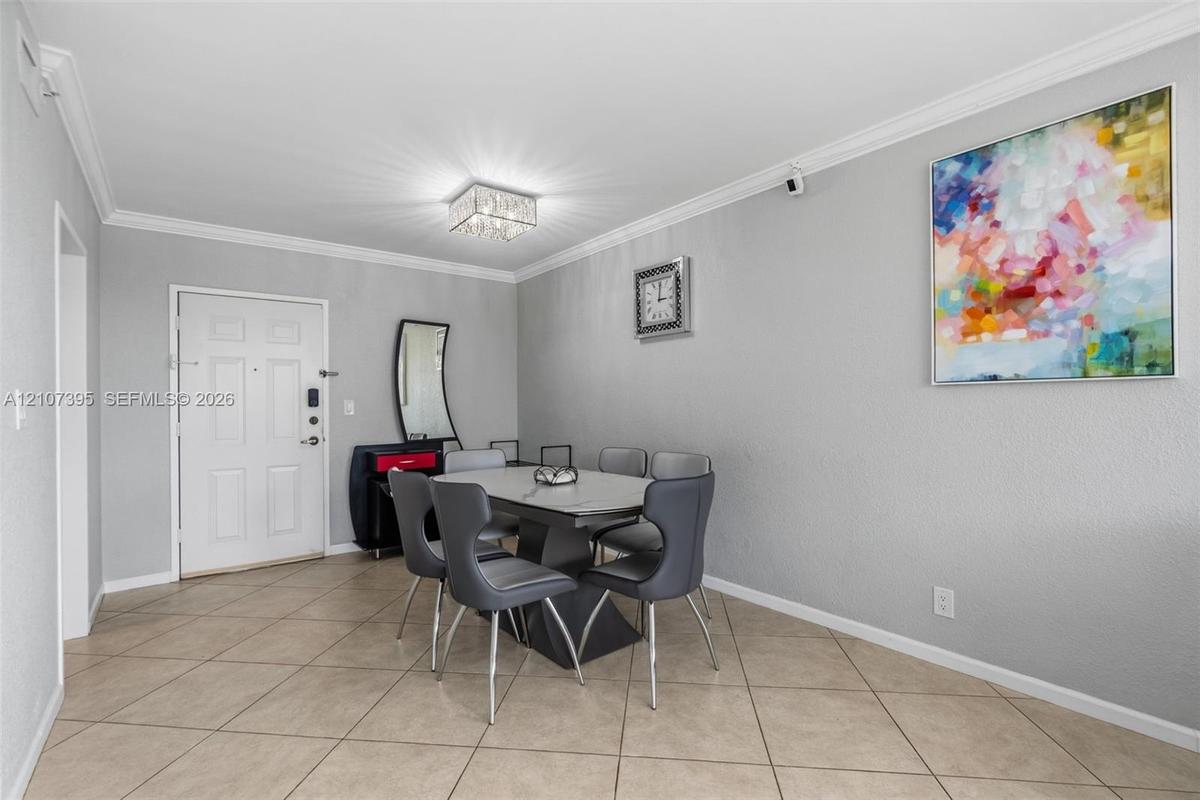 Neutral-toned room featuring crown molding, neutral tile flooring, and a crystal-accented flush mount ceiling light