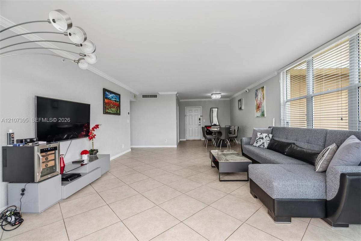 Open-concept interior featuring large-format diagonal tile flooring, crown molding, multi-arm arched floor lighting, and expansive windows with horizo