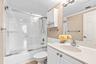 Bathroom featuring a white vanity cabinet with an integrated sink, polished chrome faucet, glass-enclosed shower and tub combination with tile surroun