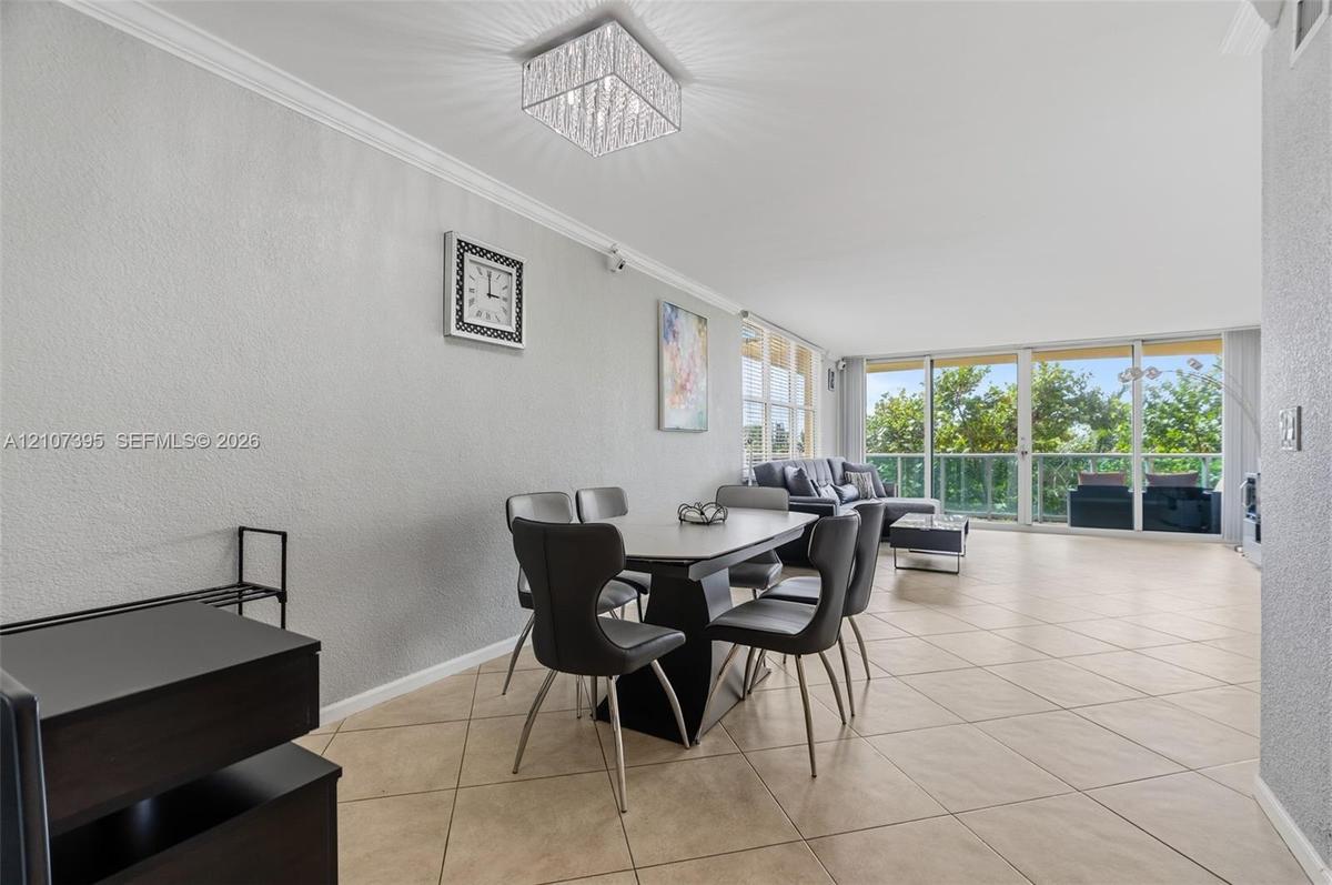Open-concept interior featuring large-format tile flooring, crown molding, a crystal-accented flush mount light fixture, and floor-to-ceiling glass sl