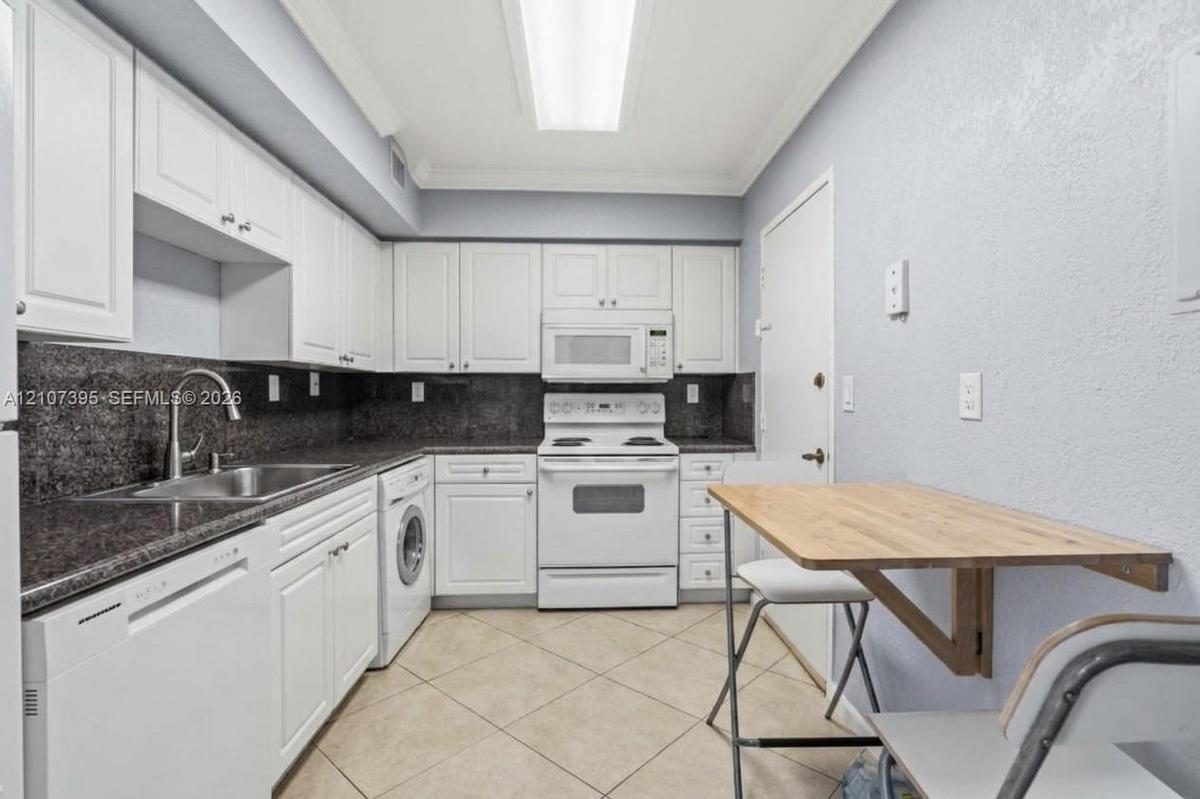 Kitchen featuring white cabinetry, dark stone-finish countertops, tile flooring, integrated appliances, and a mounted drop-leaf table