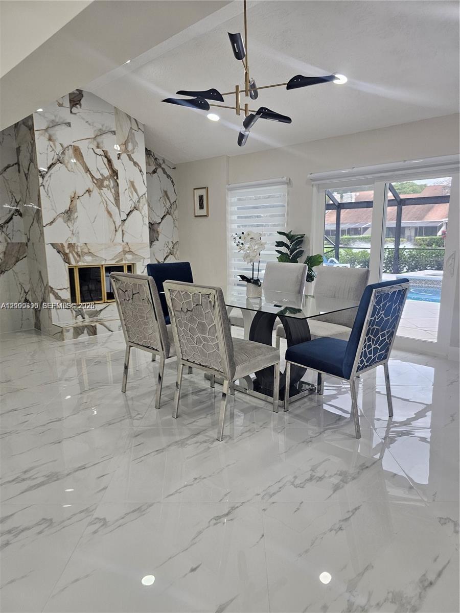 Floor-to-ceiling stone fireplace surround, polished large-format tile flooring, modern multi-arm chandelier, and sliding glass doors with access to an