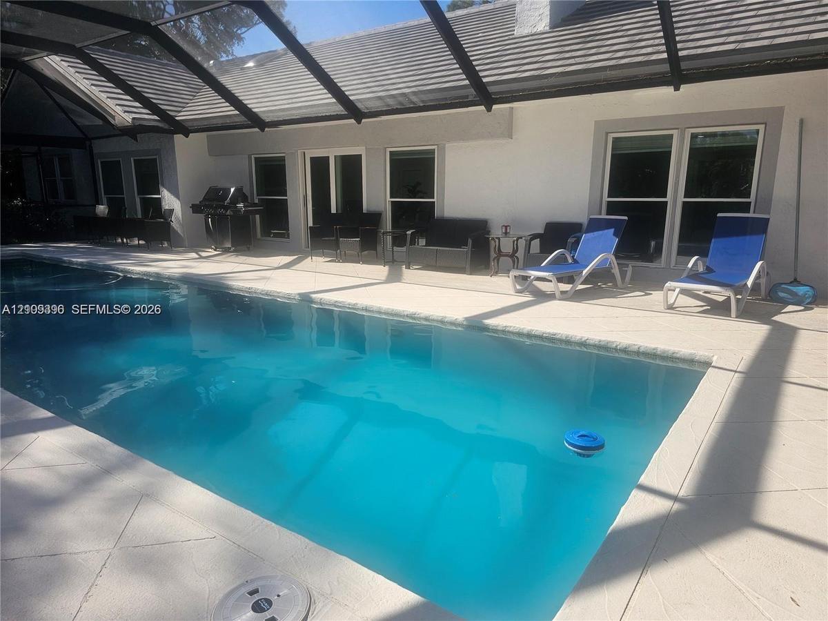 Screen-enclosed pool deck featuring a rectangular swimming pool, light-toned paved decking, and multiple exterior access points