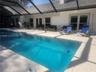Screen-enclosed pool deck featuring a rectangular swimming pool, light-toned paved decking, and multiple exterior access points