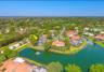 Aerial perspective of a waterfront property featuring a screened-in pool enclosure, tile roofing, and mature perimeter landscaping