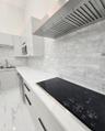 Contemporary kitchen featuring high-gloss cabinetry, stone-finish countertops, subway tile backsplash, a stainless steel range hood, and integrated el