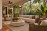 Screened-in outdoor living space featuring arched openings, stacked stone columns, tile flooring, and an integrated ceiling fan