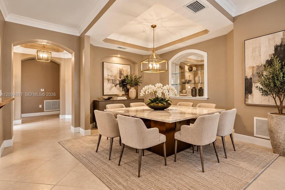 Dining area featuring a tray ceiling, recessed alcove with glass shelving, arched entryways, and crown molding