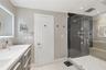 Bathroom featuring a dual-sink vanity with light-toned countertop, walk-in shower with glass enclosure, integrated bench seating, and recessed ceiling