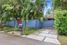 Private gated entry featuring a custom blue vertical-board fence, concrete paver driveway with crushed stone detailing, and mature tropical landscapin
