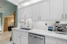 Kitchen featuring white cabinetry, solid-surface countertops, subway tile backsplash, stainless steel dishwasher, and gooseneck faucet