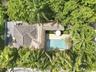 Aerial perspective featuring a rectangular swimming pool, stone-paved patio, thatched roof structure, and lush mature trees
