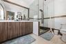 Dual-sink vanity with wood-finish cabinetry, full-width mirror, walk-in shower with frameless glass enclosure, and stone-tile flooring