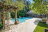 In-ground swimming pool featuring a stone-paver deck, custom wood pergola, and a thatched-roof cabana structure
