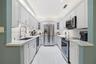 Galley kitchen featuring white cabinetry, light-toned stone-finish countertops, stainless steel appliances, a white tile backsplash, and recessed ligh