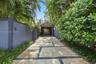 Concrete slab driveway with stone inlay, wood-paneled privacy fencing, mature landscaping, and a thatched-roof entryway structure