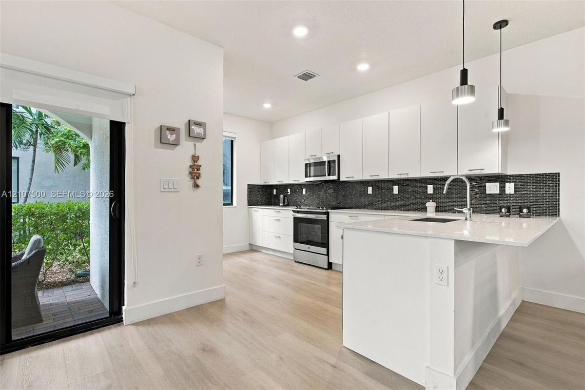 Kitchen featuring flat-panel white cabinetry, stone-finish countertops, stainless steel appliances, a dark mosaic tile backsplash, and wood-finish flo