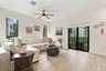 Neutral-toned living space featuring light-colored wood-finish flooring, a ceiling fan with integrated lighting, dual vertical windows, and a sliding 