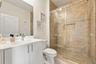 Bathroom featuring a white vanity with a rectangular sink, a frameless glass shower enclosure with sliding hardware, stone-finish wall tile, and a rec