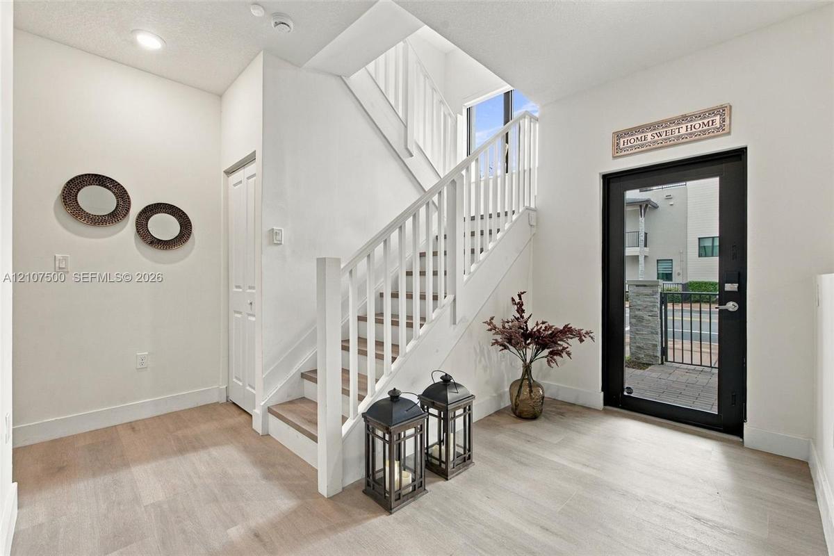 Foyer featuring wood-finish flooring, a glass-panel entry door, and a staircase with white painted balusters and wood-finish treads