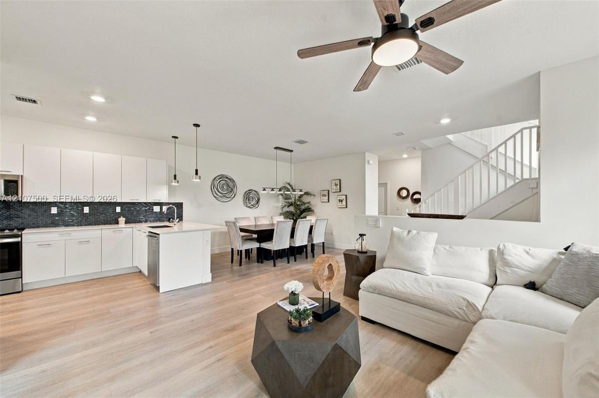 Kitchen featuring white flat-panel cabinetry, a dark tile backsplash, and a central island with countertop seating, complemented by wood-finish floori