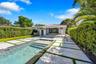 Outdoor living space featuring an in-ground pool, geometric concrete pavers with grass accents, covered patio, and perimeter privacy hedging