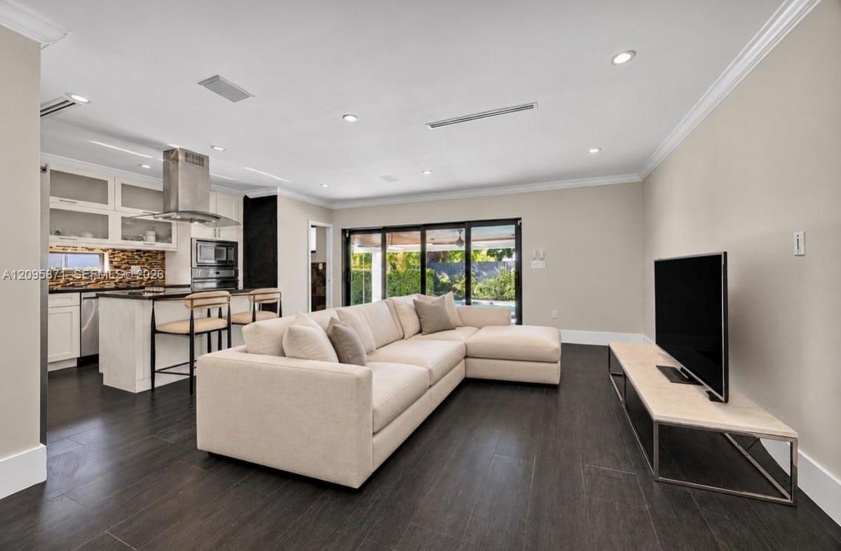 Open-concept living space featuring wood-finish flooring, recessed lighting, crown molding, and multi-panel sliding glass doors