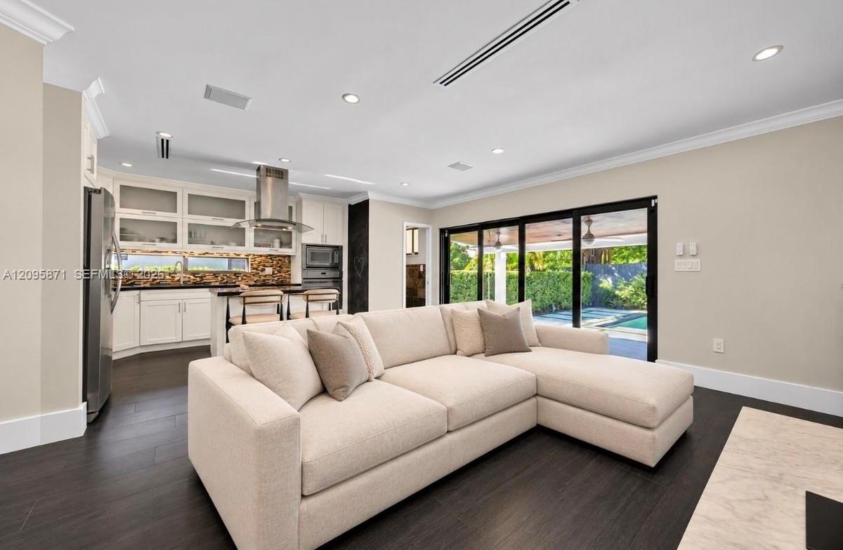 Kitchen featuring custom white cabinetry with glass-front uppers, stainless steel appliances, stone-tile backsplash, and wood-finish flooring, complem