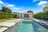 Rear exterior featuring a swimming pool with integrated stairs, concrete paver decking, perimeter privacy hedges, and a covered terrace