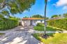 Single-story residence featuring a tile roof, light-toned stucco exterior, paver driveway, and dense perimeter hedging
