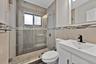 Walk-in shower with a glass enclosure, pebble-stone flooring, and decorative tile accents, paired with a white vanity featuring a rectangular basin an