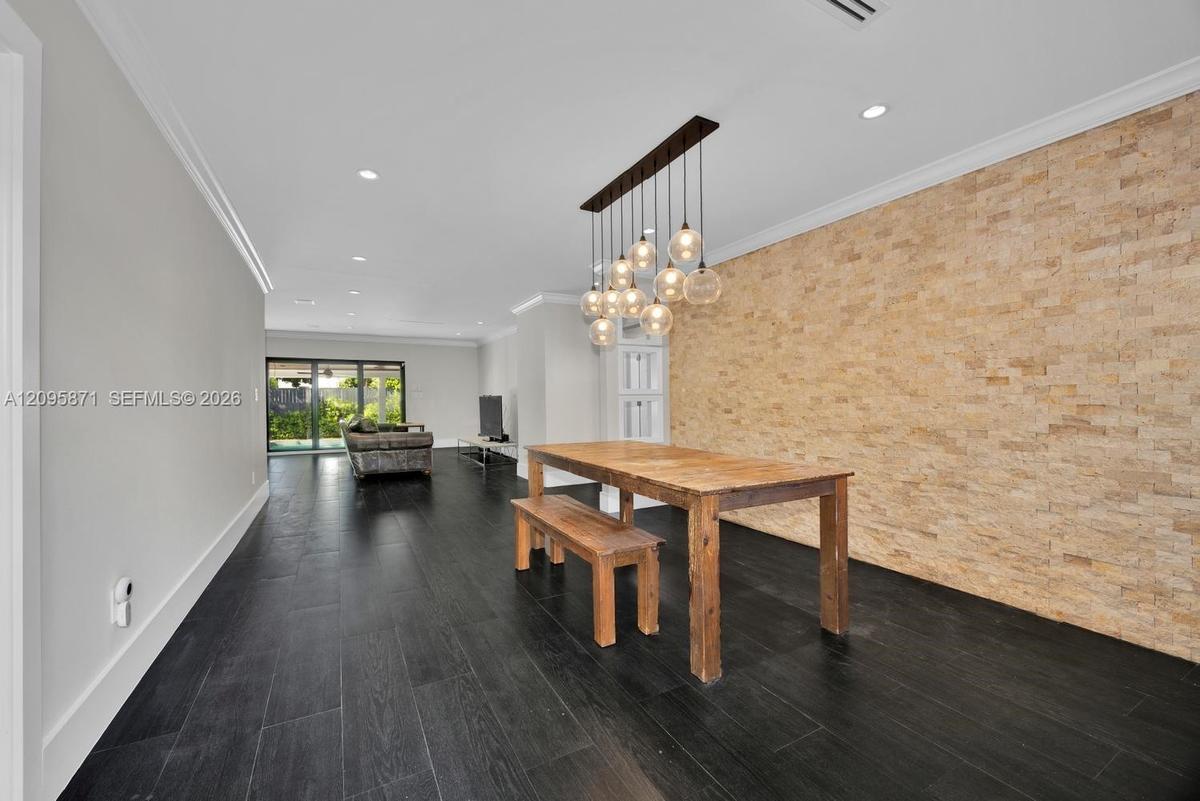 Textured stone accent wall, multi-pendant light fixture, wood-finish flooring, and recessed ceiling lighting