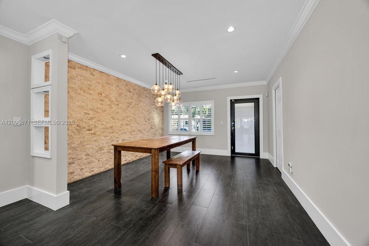 Textured stone accent wall, multi-pendant light fixture, wood-finish flooring, built-in display shelving, and plantation shutters